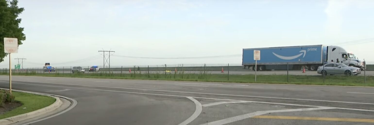 Image of an Amazon semi-truck involved in a crash on I-75 in Weston, with police cars and traffic cones near the scene.